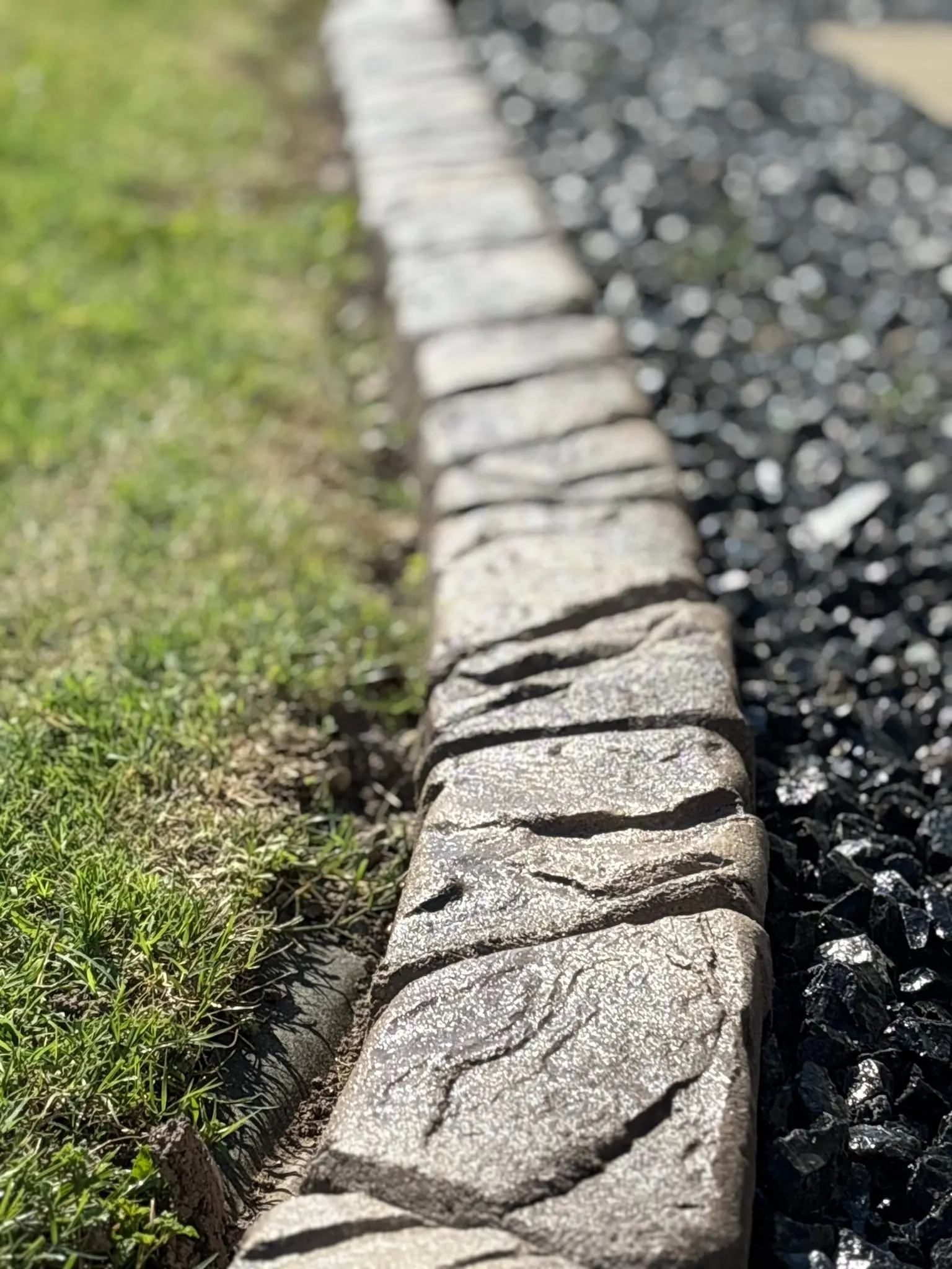 Decorative stamped concrete curbing edging a manicured flower bed installed by The Muscle
