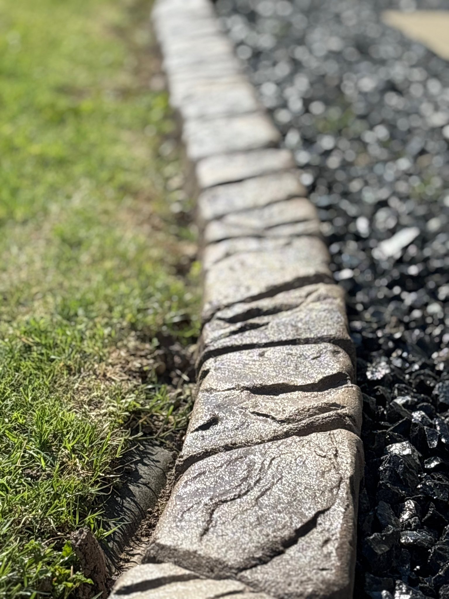 Decorative stamped concrete curbing edging a manicured flower bed installed by The Muscle